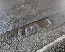 Un bache profundo y peligroso en el asfalto de una autopista de California durante el día, con coches pasando borrosos de fondo.